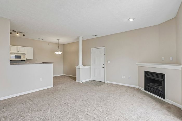 Inviting living space with plush carpeting, an elegant fireplace, and a modern open-plan kitchen with stylish lighting.