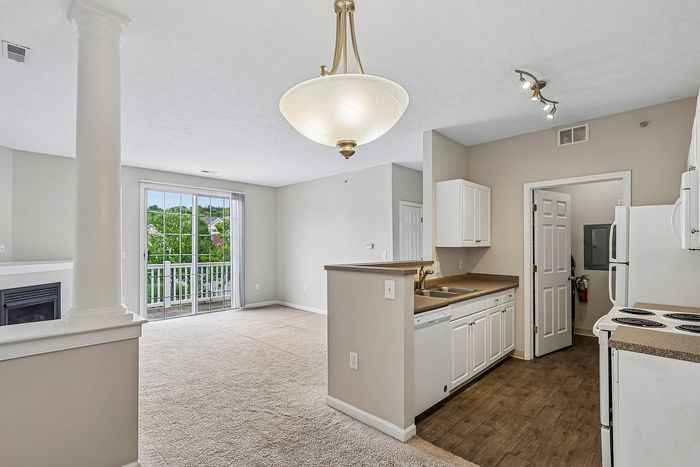 Bright and inviting apartment interior featuring a modern kitchen with white cabinetry, open living space, and large glass doors leading to a scenic balcony.