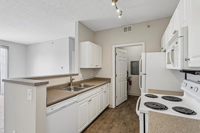 Bright and modern kitchen with sleek countertops, white cabinetry, and convenient appliances, opening into a spacious living area.