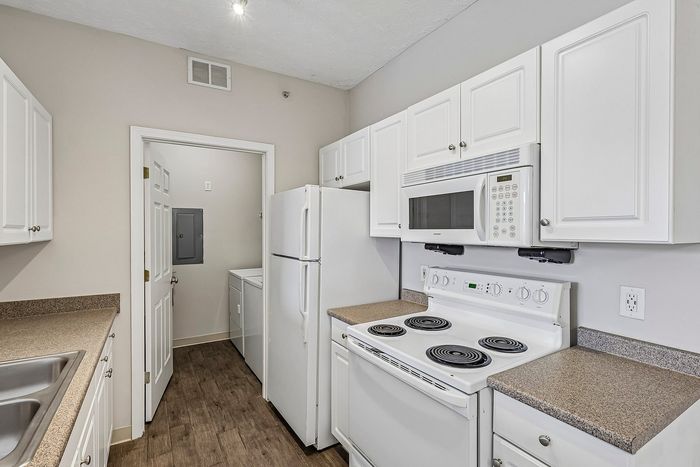Bright, modern kitchen with white cabinetry, sleek appliances, and elegant countertops, leading to a convenient laundry area.