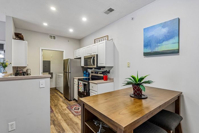 Modern kitchen with white cabinetry, stainless steel appliances, elegant wood flooring, and accent lighting.