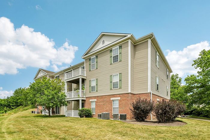 Charming three-story apartment building with a spacious balcony, surrounded by lush greenery and a clear blue sky.