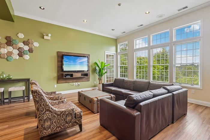 Bright and inviting living room with large windows, plush leather seating, and modern decor, featuring a stylish green accent wall.