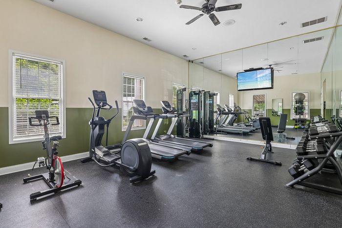 Modern apartment gym with state-of-the-art equipment, including treadmills, stationary bike, and weight racks, complemented by large mirrors and natural light.