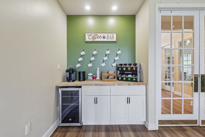 Charming home coffee bar setup with elegant green accent wall, hanging mugs, and modern brewing station.