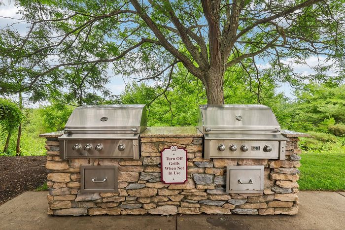 Charming outdoor stone kitchen with dual stainless steel grills set against lush greenery, ideal for summer barbecues.