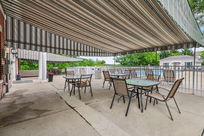 Inviting outdoor patio featuring comfortable seating, under a stylish canopy, adjacent to a sparkling swimming pool.