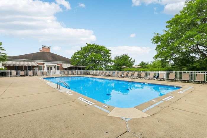 Inviting outdoor pool area with rows of sun loungers, set against a beautifully landscaped backdrop featuring lush greenery and clear blue skies.