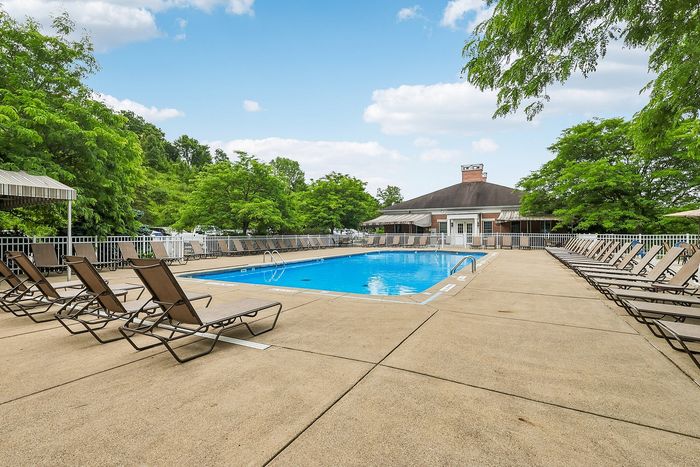 Inviting outdoor pool area with numerous lounge chairs, surrounded by lush greenery and a charming clubhouse.