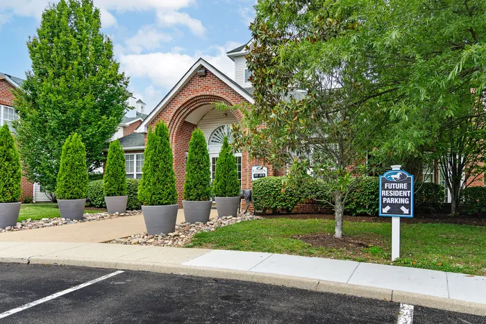 Charming brick-faced apartment complex entrance with lush greenery and a welcoming pathway for future residents.