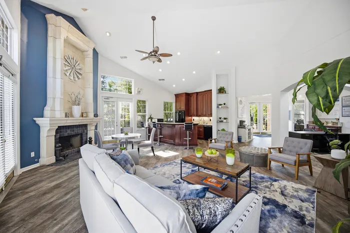 Elegant open-concept living space with a vaulted ceiling, featuring a cozy fireplace, modern kitchen with dark wood cabinetry, and abundant natural light, perfect for stylish entertaining.