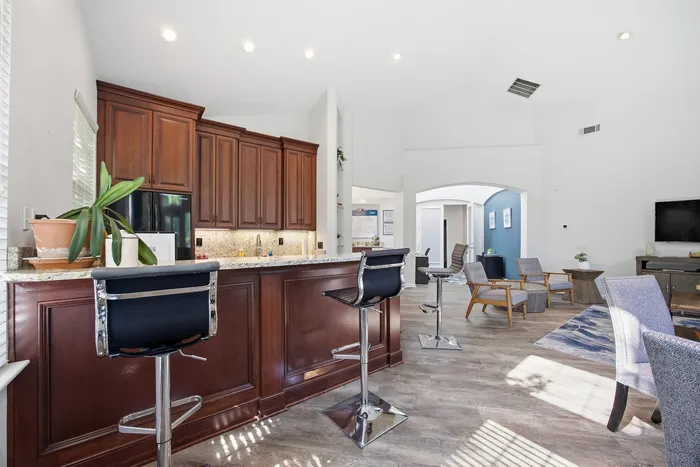 Elegant open-concept living area featuring a gourmet kitchen with rich wooden cabinetry, granite countertops, and modern bar seating, flowing into a stylish, sunlit living space.