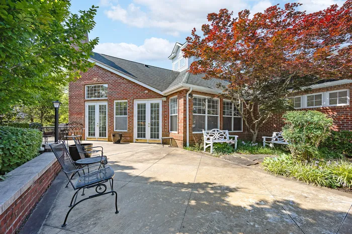 Charming brick exterior with lush landscaping and cozy outdoor seating, highlighted by vibrant foliage and elegant French doors.