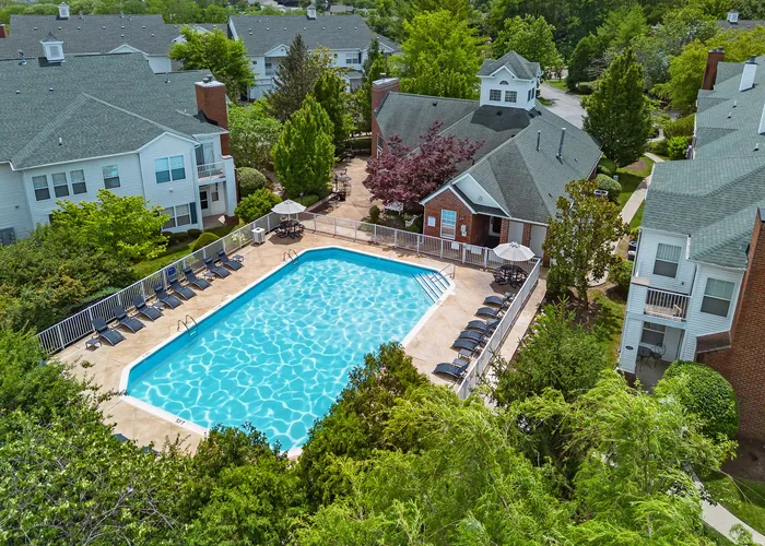 Inviting aerial view of a luxurious apartment complex with a sparkling swimming pool, surrounded by lush greenery and comfortable lounge chairs for relaxation.