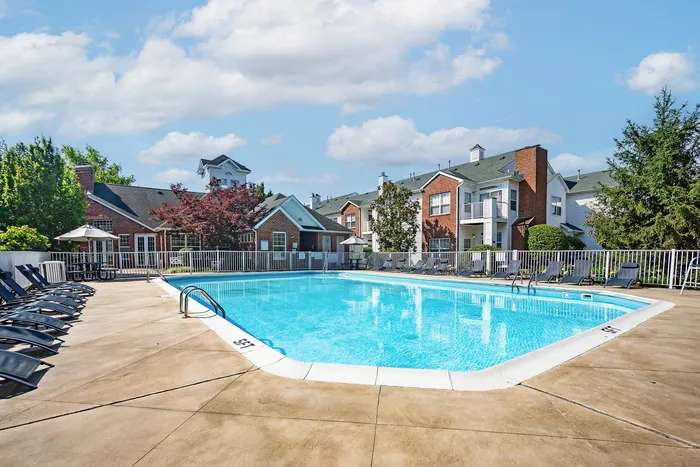 Inviting apartment complex with a sparkling outdoor pool, surrounded by lounge chairs and lush landscaping.