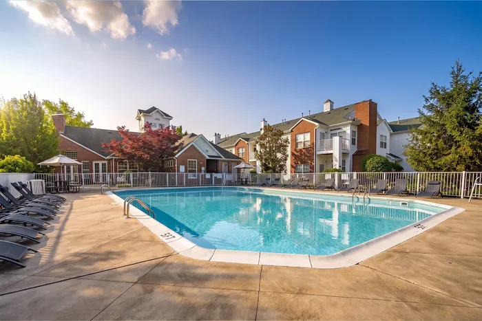 Luxurious apartment complex with a sparkling outdoor swimming pool, surrounded by modern brick buildings and lush greenery, perfect for relaxation and leisure.