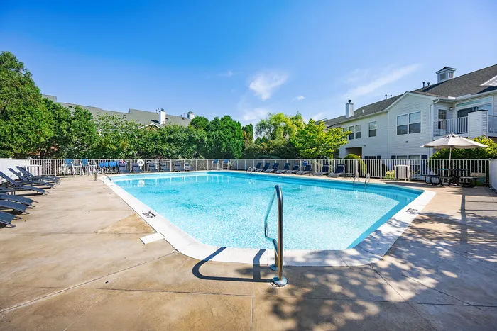 Inviting outdoor swimming pool surrounded by lounge chairs and lush greenery in a serene apartment community setting.