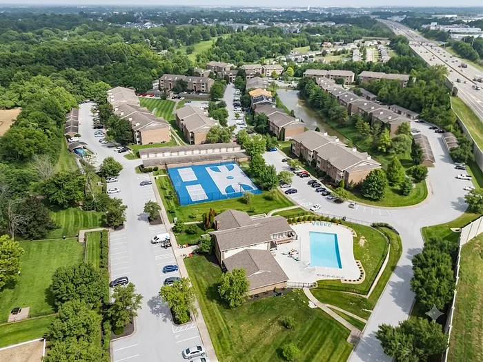 Aerial view of a vibrant apartment complex with lush greenery, spacious pool, and tennis courts, offering a harmonious blend of nature and modern amenities.