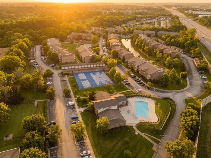 A picturesque aerial view of a modern apartment complex surrounded by lush greenery, featuring a sparkling swimming pool and basketball courts under a golden sunset.