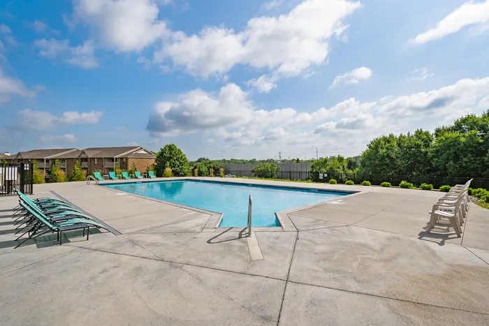 Serene outdoor pool area with comfortable lounge chairs, surrounded by lush greenery under a clear blue sky.