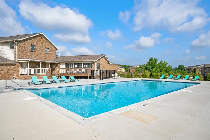 Inviting outdoor pool area with sun loungers, set against a backdrop of lush greenery and charming brick architecture.