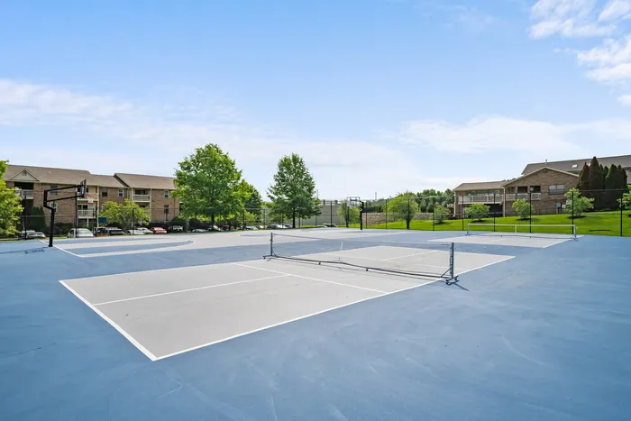 Vibrant outdoor sports area with tennis court and basketball hoop, surrounded by lush greenery and modern apartments.