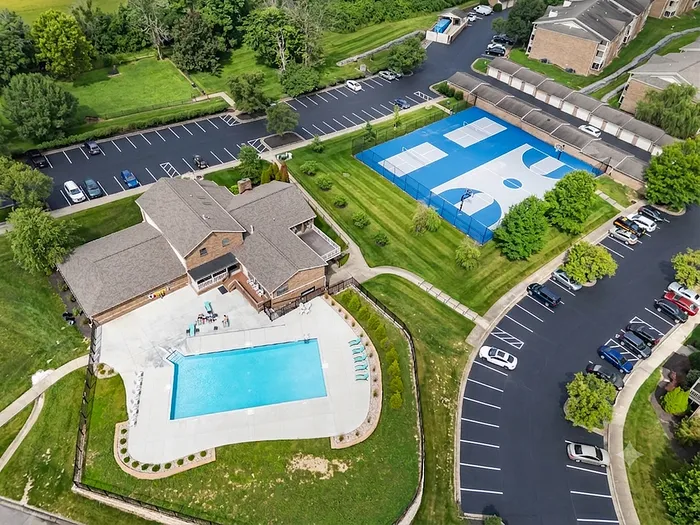 Stunning aerial view of a modern apartment complex featuring an inviting swimming pool, lush green spaces, and a well-maintained basketball court, perfect for leisure and recreation.