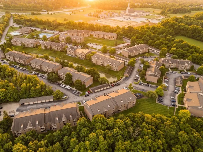 Serene aerial view of a picturesque apartment complex nestled in lush greenery, radiating a warm, inviting ambiance at sunset.
