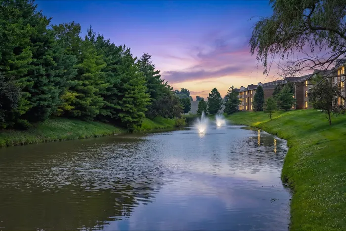 Scenic lakeside view at dusk featuring elegant fountains, lush greenery, and modern apartments reflecting a serene waterfront lifestyle.