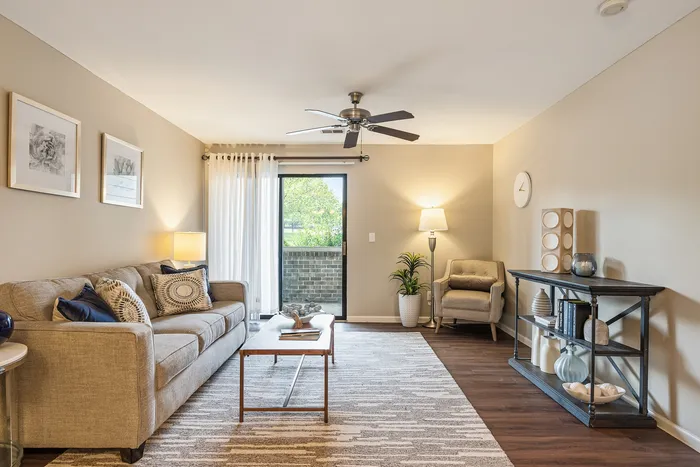 Charming living room with contemporary decor, plush sofa, stylish armchair, and natural light from a large glass door leading to a private balcony.