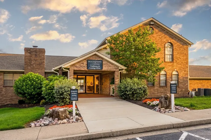 Charming entrance to the leasing office, surrounded by lush landscaping and vibrant flowers under a picturesque sky.