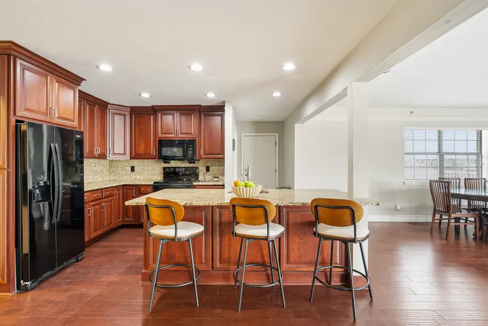Elegant open-concept kitchen featuring rich wooden cabinetry, granite countertops, and a spacious island with seating overlooking a bright dining area.