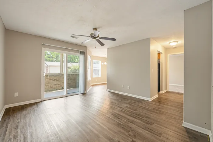 Bright and inviting living room with elegant wood flooring, ceiling fan, and large sliding glass doors leading to a cozy balcony.