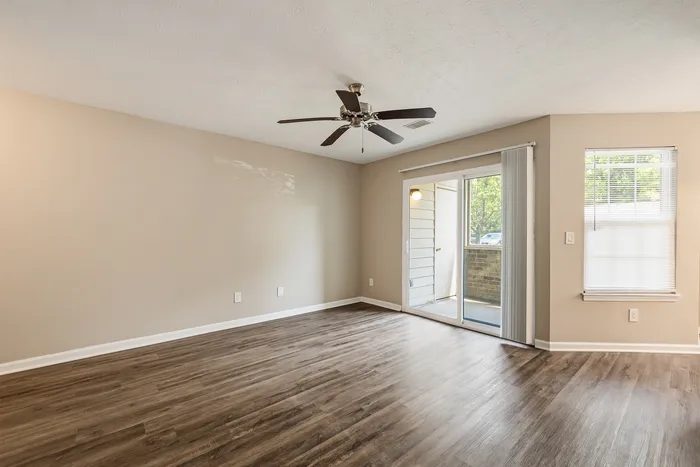 Elegant living room with modern wood flooring, ceiling fan, and natural light through large patio doors, creating a bright and inviting space.