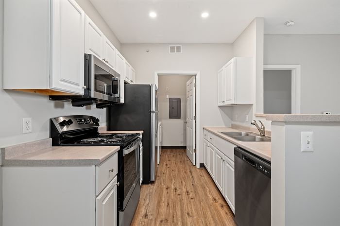 Modern kitchen with sleek white cabinets, stainless steel appliances, and elegant wood flooring.