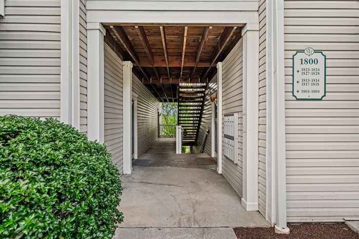 Modern apartment entrance with clean lines, natural wood accents, and lush greenery, inviting residents to a serene living experience.