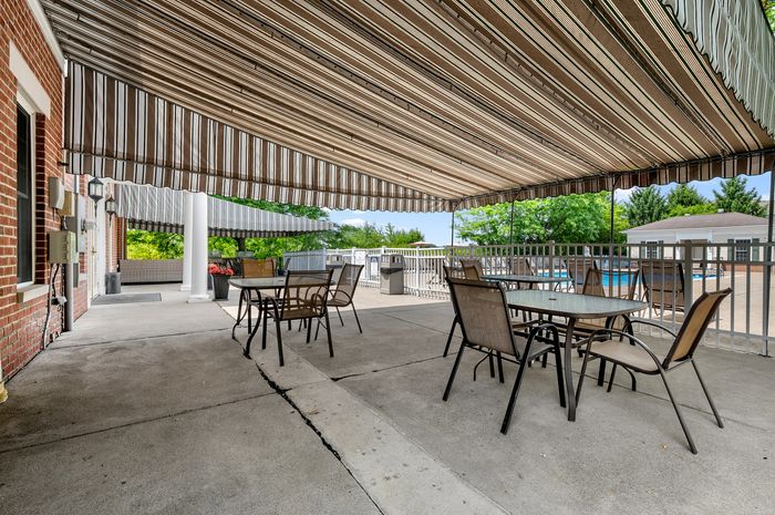 Inviting outdoor patio with modern chairs and tables under a stylish striped awning, overlooking a refreshing pool area.