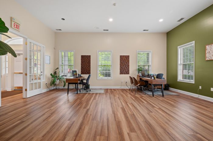 Elegant office space with stylish hardwood flooring, natural light from large windows, and modern decor, offering a welcoming and professional environment.