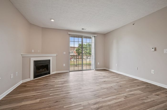Bright living room with modern hardwood floors, cozy corner fireplace, and large sliding glass doors leading to a scenic balcony.