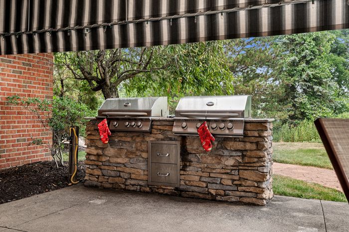 Charming outdoor kitchen with dual stainless steel grills on a rustic stone base, surrounded by lush greenery, perfect for entertaining.