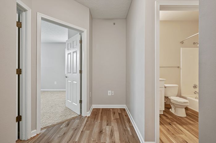 Inviting hallway with elegant wood flooring leading to a cozy carpeted bedroom and a modern bathroom.