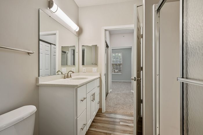 Modern bathroom with sleek white vanity, elegant fixtures, and access to a bright adjoining bedroom.