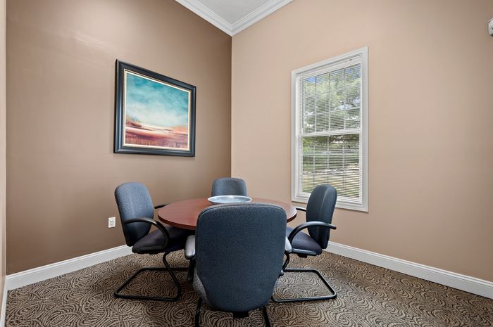 Inviting meeting room with a round wooden table, four comfortable chairs, and a large window providing natural light.