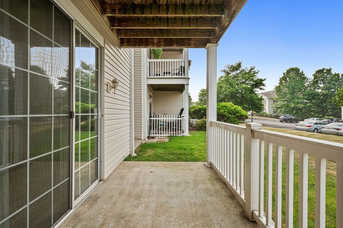 Charming ground-level patio with cozy outdoor space, overlooking lush greenery and a peaceful residential street.