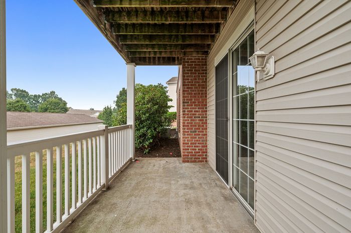 Inviting apartment balcony with elegant brick and siding finish, overlooking lush greenery and open skies, perfect for relaxation.