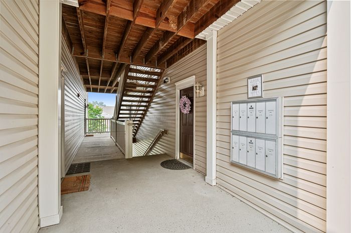 Inviting apartment entrance with modern mailboxes and rustic wooden ceiling, featuring natural light and a welcoming wreath on the door.