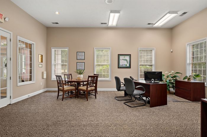 Elegant office space with natural light, featuring a cozy meeting area with a round wooden table, stylish chairs, and modern workstations.