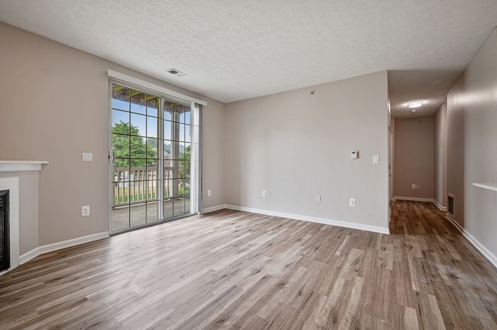 Bright living area with elegant hardwood floors, expansive sliding glass doors leading to a serene outdoor space, and warm, neutral walls.