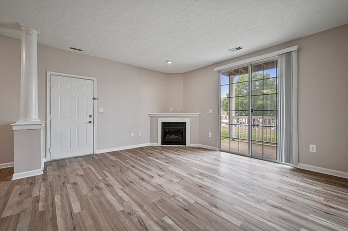 Bright, modern living area with elegant flooring, cozy corner fireplace, and expansive sliding glass doors opening to a balcony.