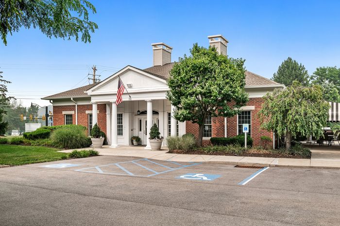 Charming brick clubhouse with classic pillars and lush landscaping, featuring convenient handicap parking.